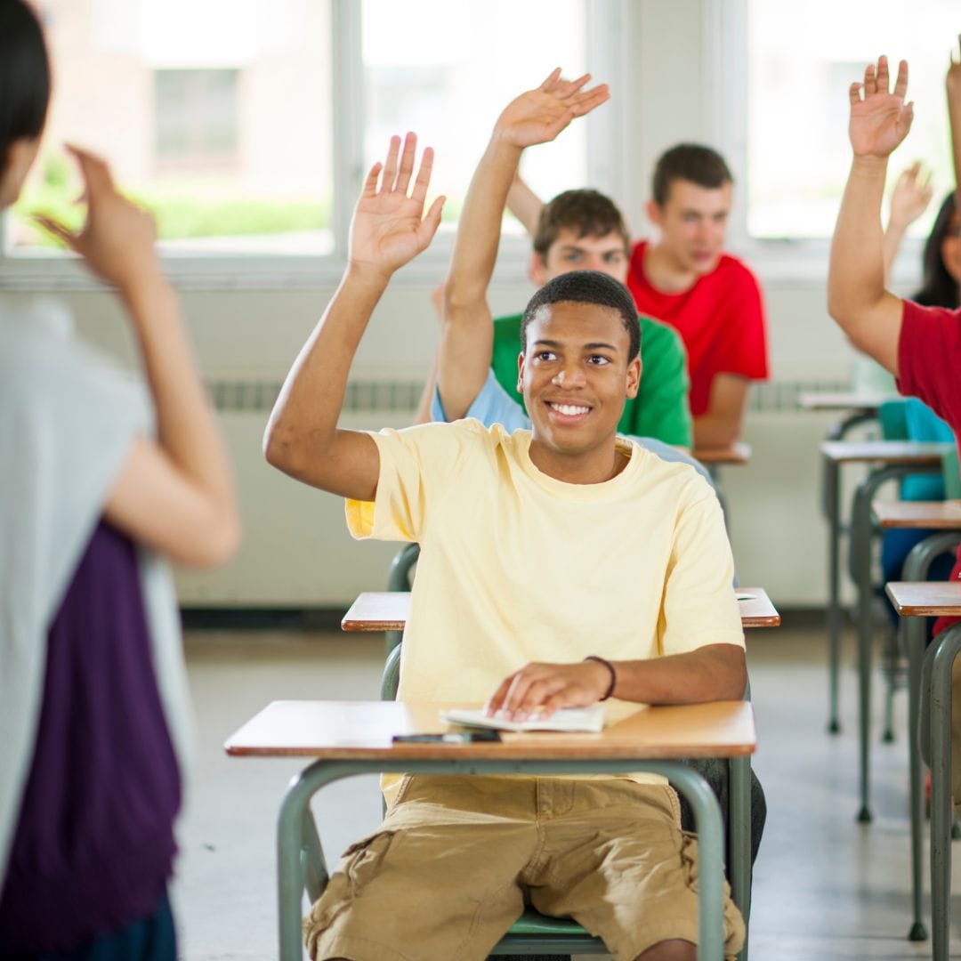 Élève levant la main en étant assis sur son bureau dans la classe à l'école